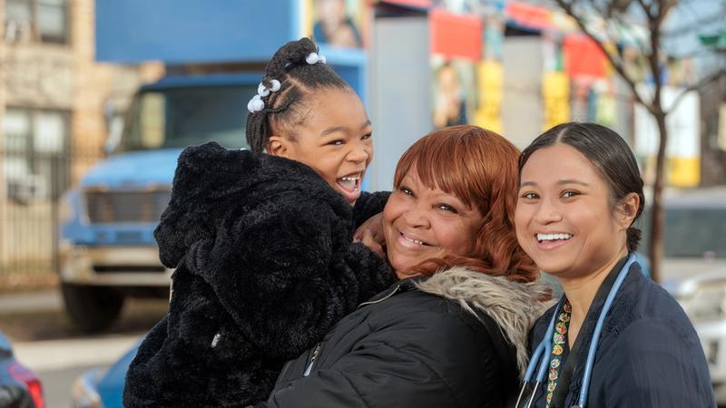 A nurse from MedStar Health poses for a photo with a mother and her daughter with the MedStar mobile health truck in the background.