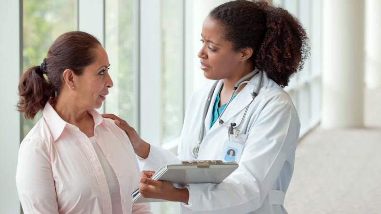 A doctor talks with a patient in an office hallway.