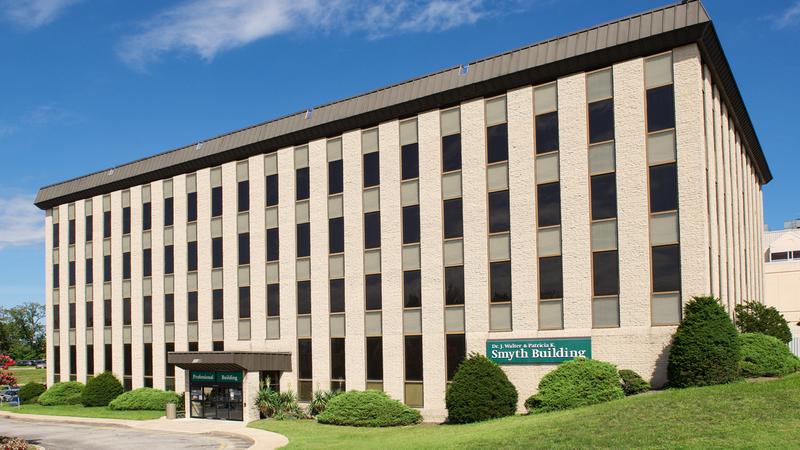 The Smyth Building on the campus of MedStar Good Samaritan Hospital in Baltimore, is a late-20th century concrete and glass building with a green sign.