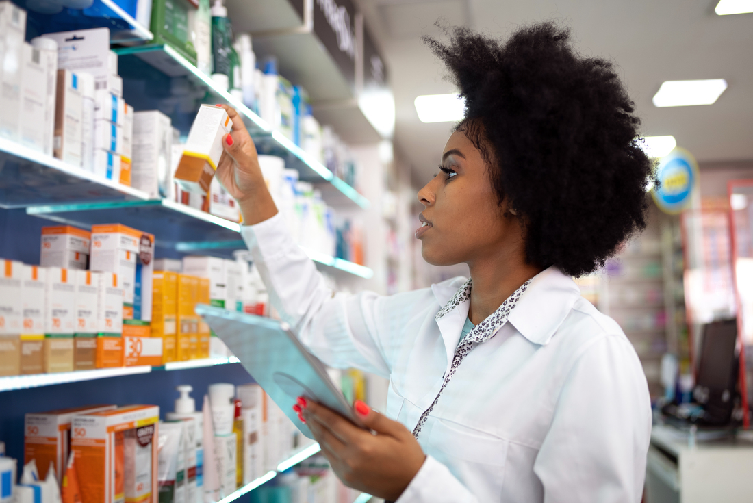 A young female pharmacist reads the label on a box of medication inside of a pharamcy.