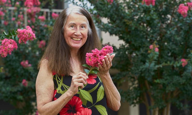 Marcia Bachman, a MedStar Health patient, holds a flower in her garden while smiling at the camera.