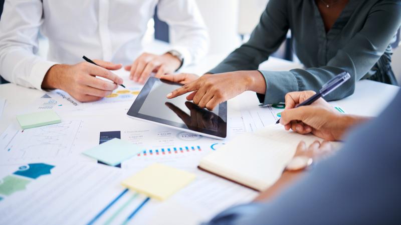 Three professionals sit at a conference table and plan.