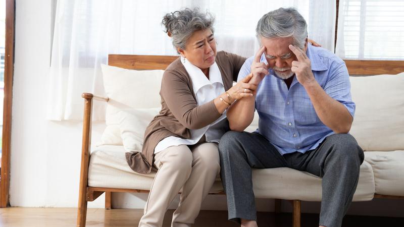 A senior woman comforts her husband who is experiencing head pain.