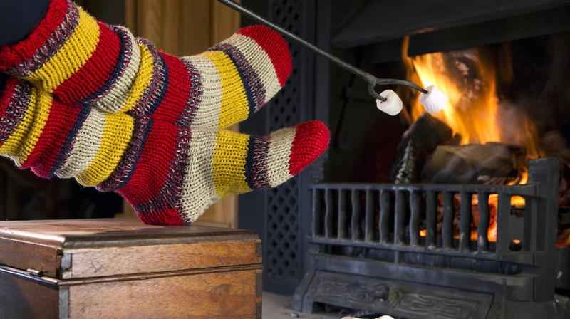 Close up of a person wearing socks warming their feet by a fireplace.