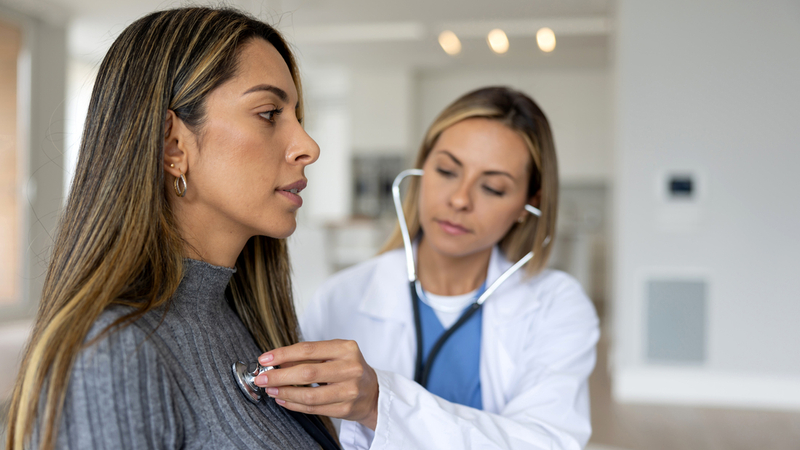 A female doctor listens to the heart of a young female patient in a clinical setting.