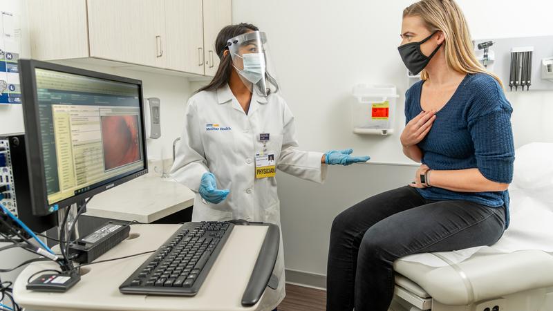 A doctor talks with a female patient who is holding her stomach in pain.