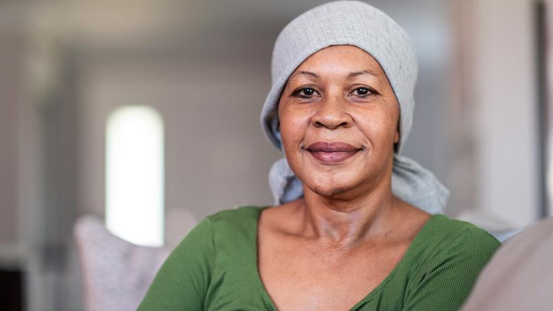 An african american woman wearing a head scarf poses for a portrait in her home.