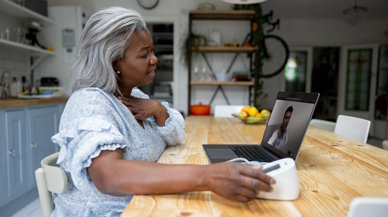 A senior woman participates in a video health visit with her doctor while sitting at her kitchen table.