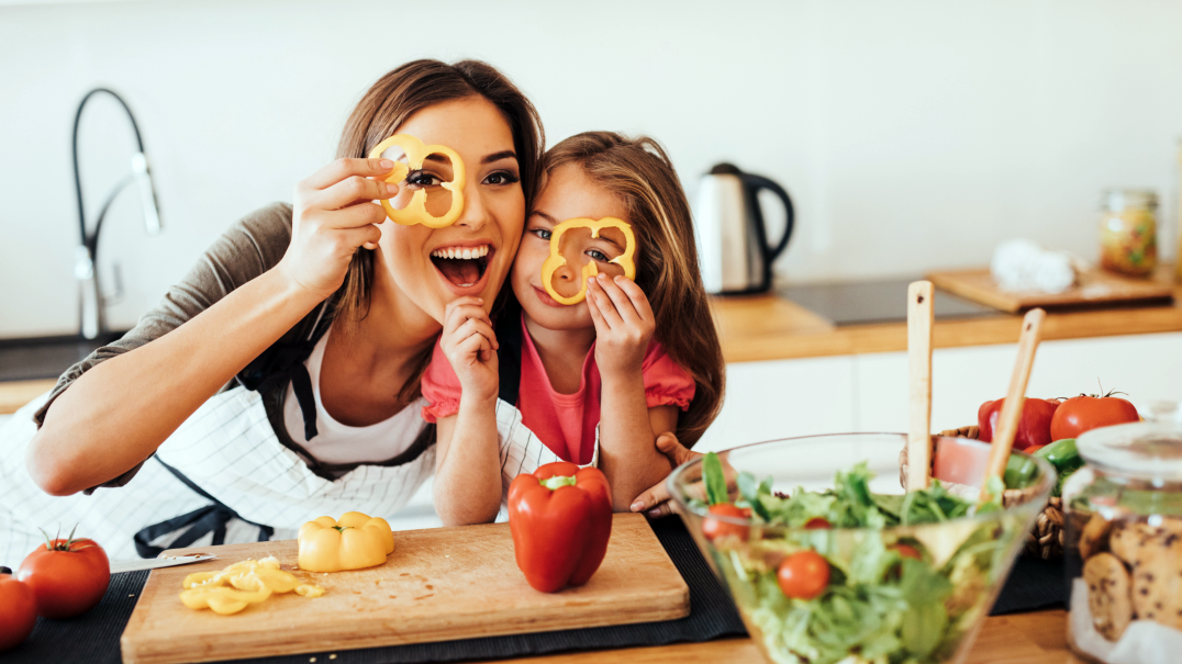 A mother and young child look through slices of peppers as they prepare a healthy salad for a meal.