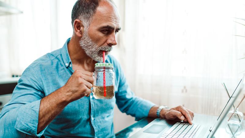 A man sits at his desk and drinks water while he works.