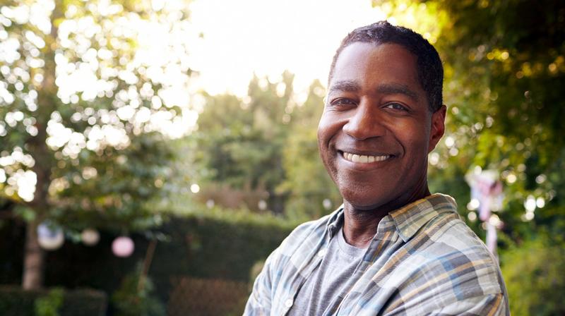 A handsome African American man poses for a photo outdoors. He is looking at the camera and smiling.
