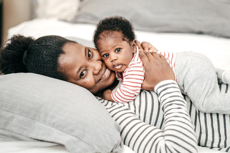 A mother lays with her baby on her chest and they smile for the camera.