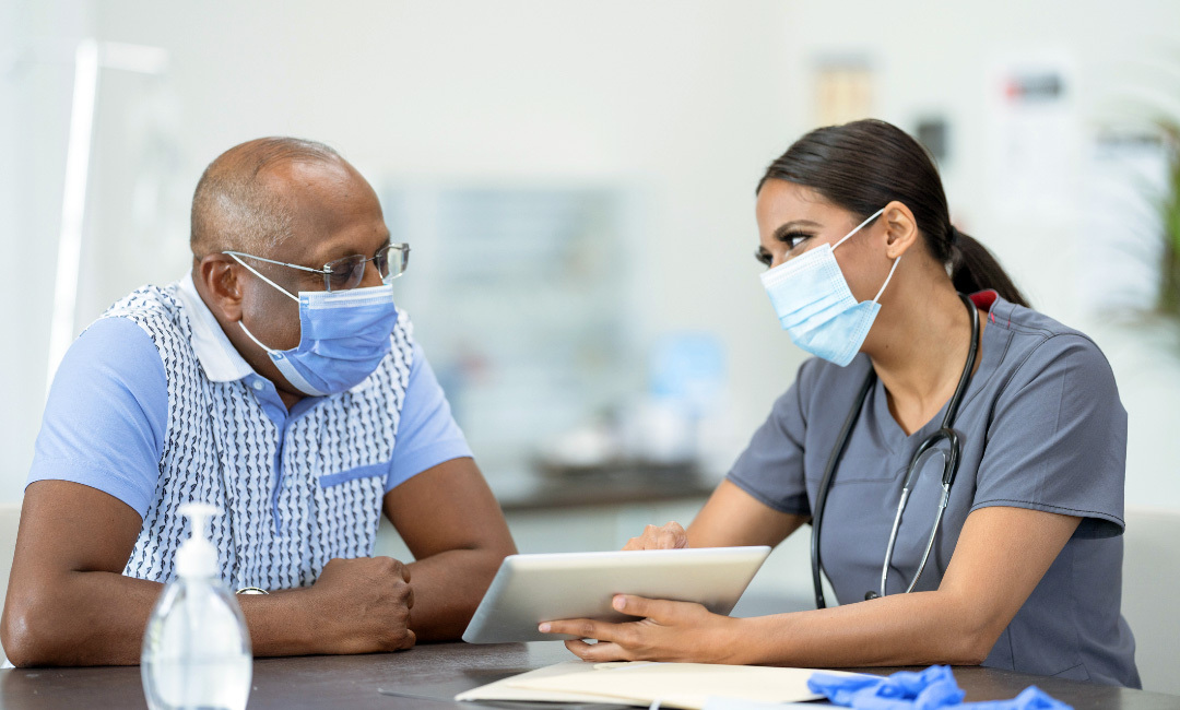 A man sits and talks with a nurse show is showing him something on an ipad.