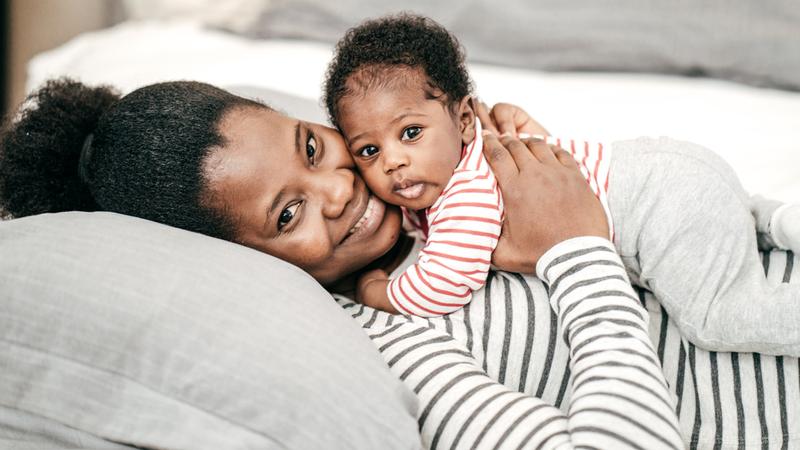 A mother lays with her baby on her chest and they smile for the camera.