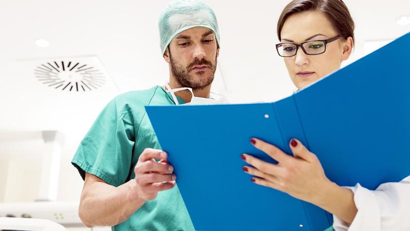 Two doctors look at a binder of papers.