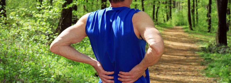 A man stretches his back while on a run in the woods.