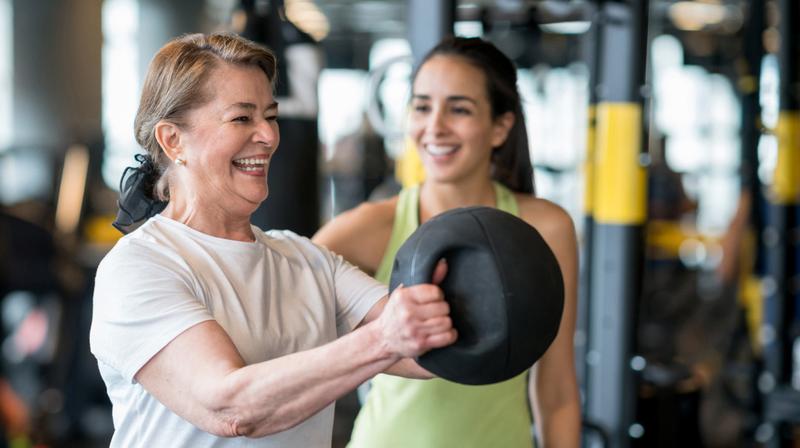 A mature woman works with a physical therapy trainer in a gym.
