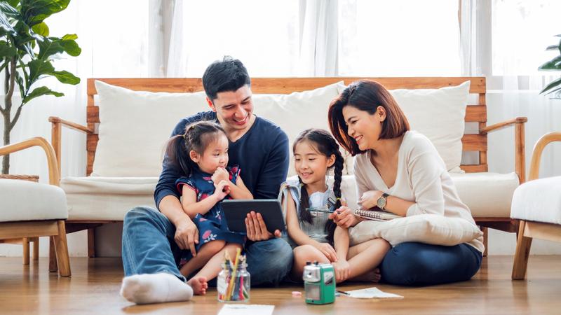 A family sits together and looks at a laptop computer on the floor in their livingroom.