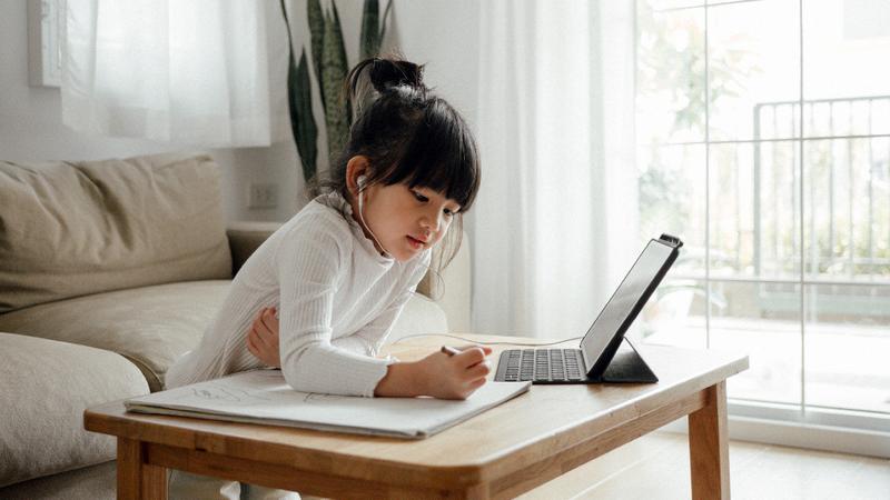 A young girl does her homework using a computer at home in her living room.