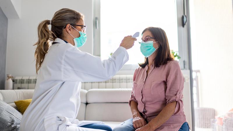 A nurse takes a patient's temperature. Both people are wearing masks.