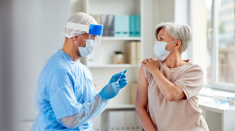 A doctor gives a flu vaccination to a patient in an office setting. Both people are wearing masks.