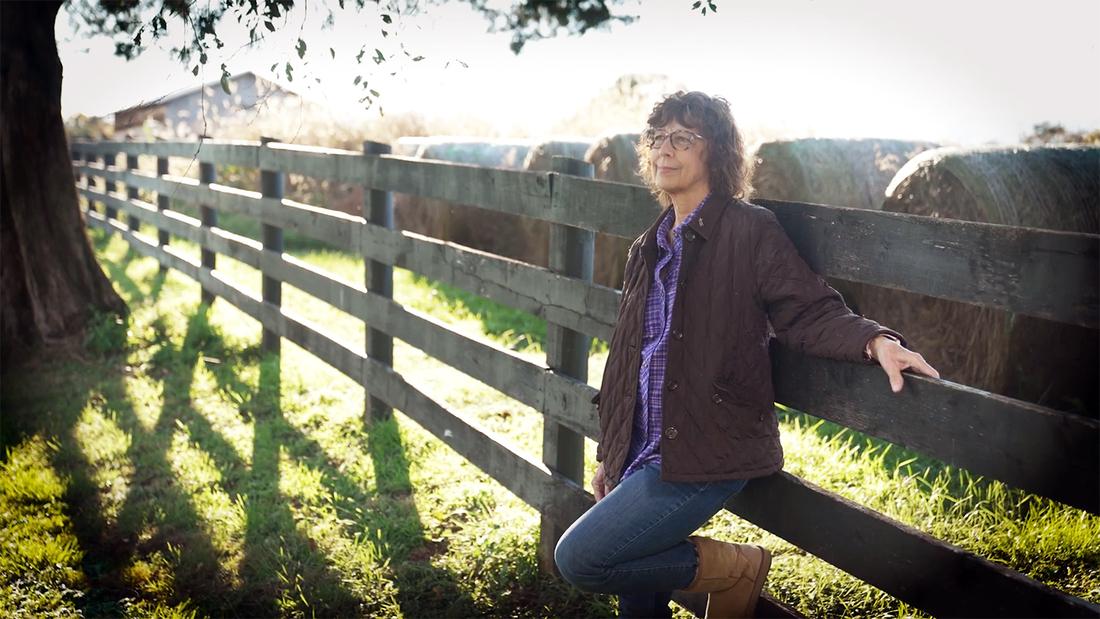 Bonnie Embreys leans against a fence on a horse farm.