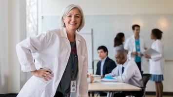 A female doctor leans on a conference table while waiting to start a staff meeting.