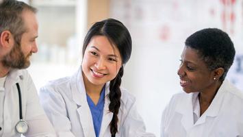 Three medical professionals talk in a hospital setting.