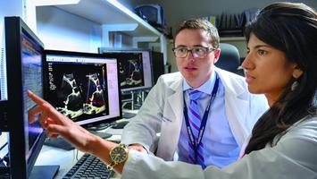 Two cardiovascular disease fellows look at a computer screen in a computer lab.