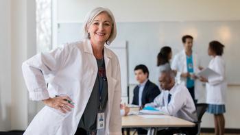 A senior female doctor leans on a conference table while waiting to start a staff meeting.