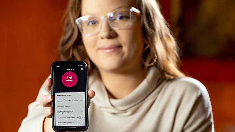 Amanda Linzau holds her phone which shows a patient monitoring app for babies.