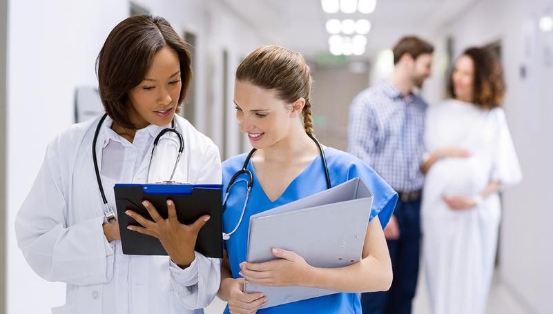 A doctor and nurse talk in a hospital hallway.