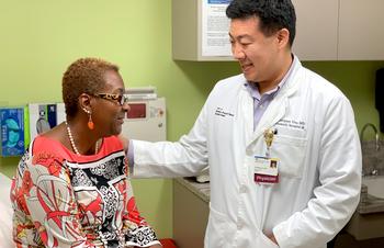 Dr. Christopher You, bariatric surgeon, consults with a female patient during an office visit at MedStar Health. The wall behind them is bright green, and Dr You has his hand on the patient's shoulder.