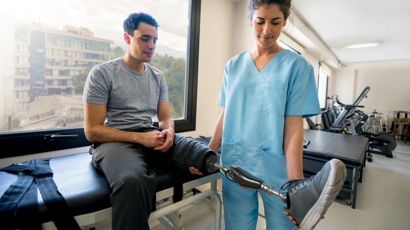 A therapist works with a patient with a prosthetic leg in a clinical setting.