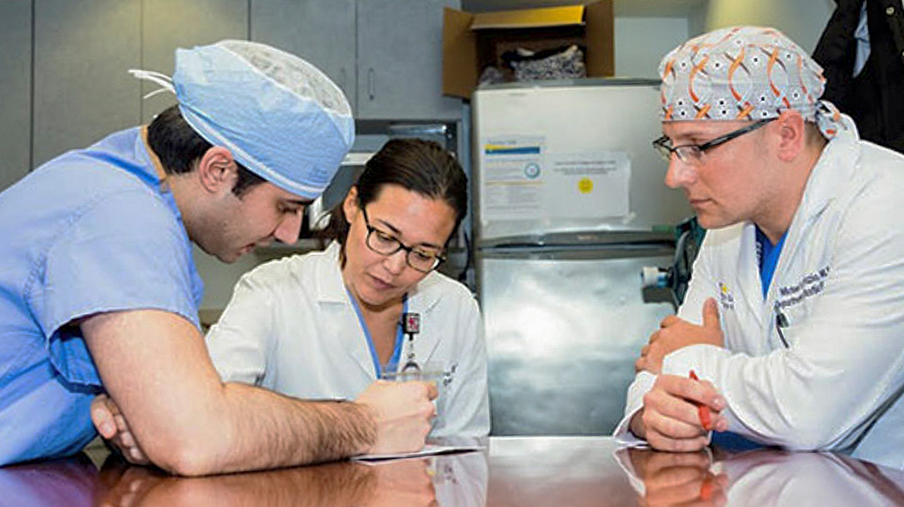 Three health professionals collaborate on a report. Two of the people are wearing surgical caps.