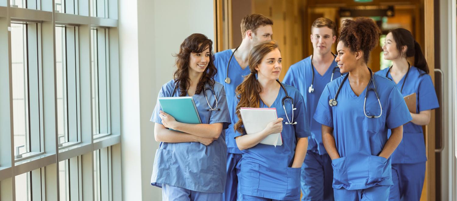 A group of medical students talk while walking down a hospital hallway.