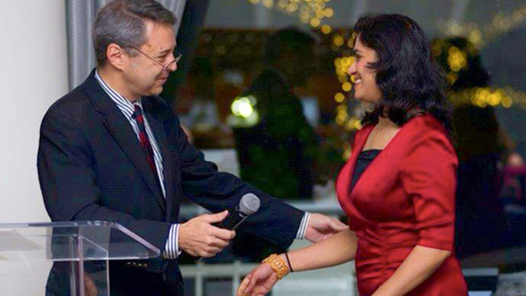 A woman in a red jacket steps up to a podium at a professional event.