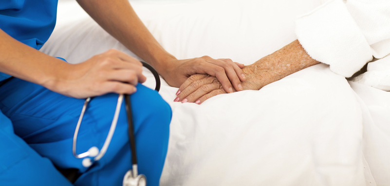 Close up photo of a nurse's hand on top of an elderly patient's hand.