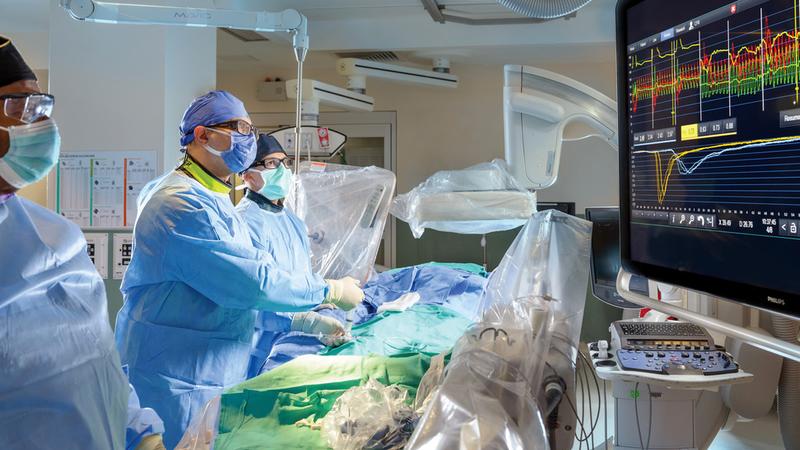 Dr Hayder Hashem and 2 assistants performs a procedure in the cardiac catheterization lab at MedStar Washington Hospital Center. All of the people are wearing masks, gloves, and full PPE.