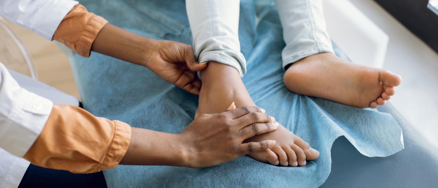 Close-up photo of a female doctor's hands examining a young person's foot injury