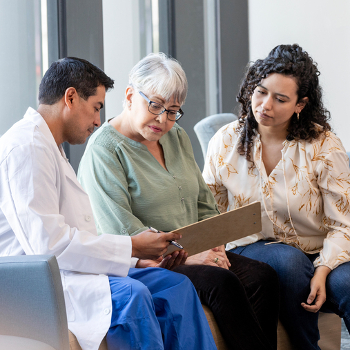 A doctor talks with a patient and her family member in a hospital setting.