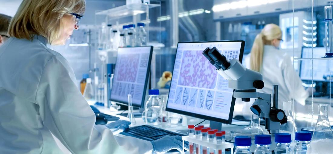 A female scientist works in a clinical laboratory and looks at cells on a computer monitor.