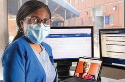 一名MedStar Health服务人员在几台电脑前合影，其中一台电脑是与一名打电话来进行远程医疗访问的女性患者合影的。