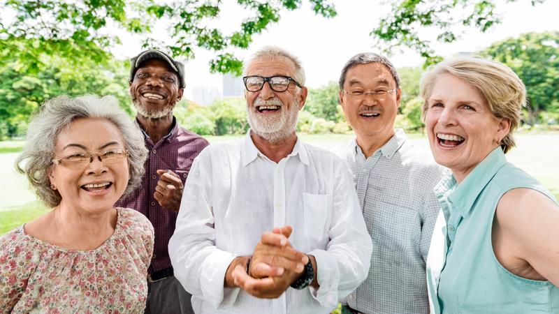 A diverse group of older adults outdoors under a tree.