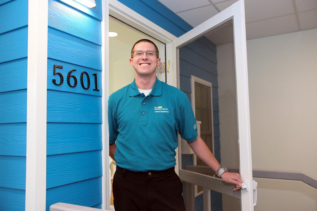 Physical Therapist Ronnie Green poses for a photo in front of a model of the front door of a home, in the rehabilitation gym at MedStar Good Samaritan Hospital.