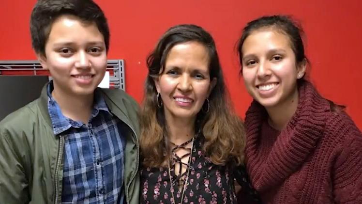 Martha Ramos, cancer survivor, stands with her arms around her 2 children. All of them are looking at the camera and smiling.