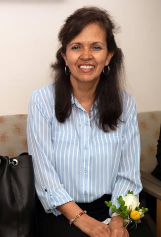 Martha Ramos sits and smiles for the camera, wearing a coursage of yellow and white roses on her wrist.