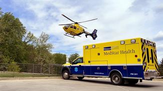 The MedStar Health helicopter flies over a parked MedStar Health ambulance.