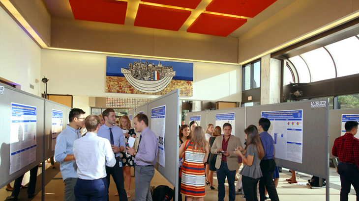 Groups of medical students stand together and chat while viewing abstract presentations at a medical conference.