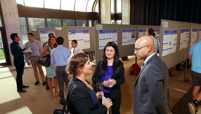 Groups of medical students stand together and chat while viewing abstract presentations at a medical conference.
